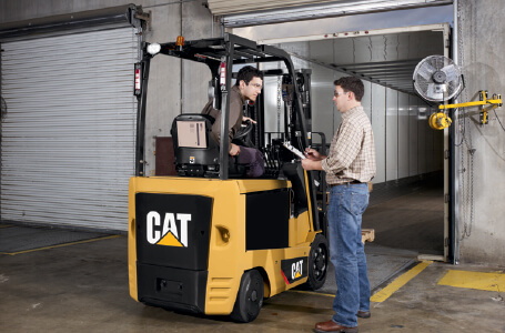 Worker with a clipboard talking with worker on Cat forklift